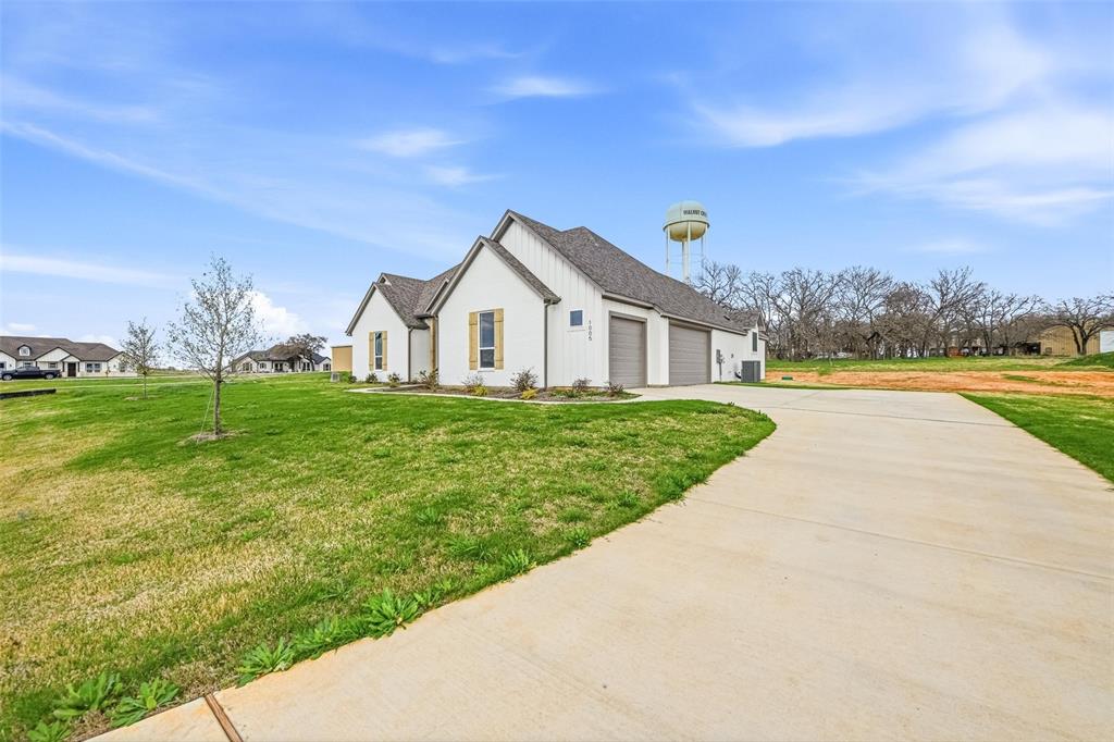 1005 Ronnie Court Springtown, TX 76082 - Photo 5 of 27 View of property exterior featuring a yard, driveway, an attached garage, roof with shingles, and board and batten siding