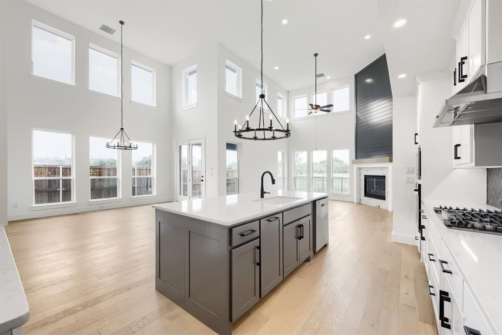 733 Red Cedar Road Haslet, TX 76052 - Photo 9 of 28 Open-concept living area featuring a kitchen island with stone countertop, wood-finish flooring, a contemporary fireplace with a shiplap accent wall, high ceilings, and abundant natural light from numerous windows