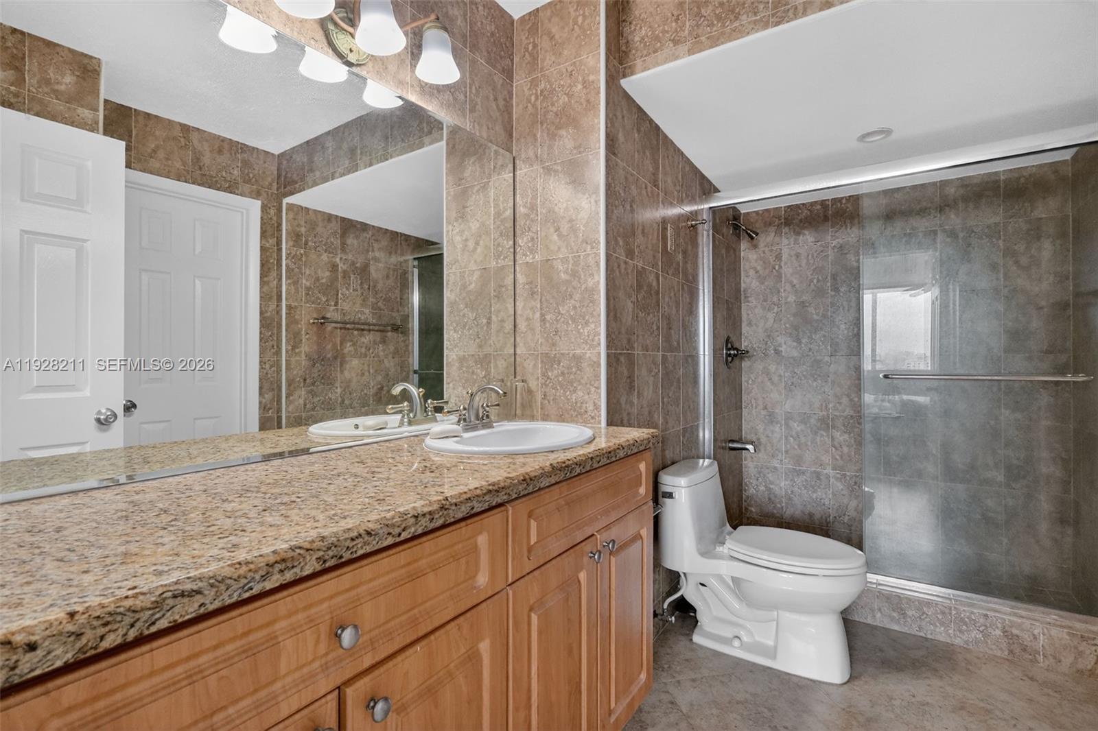 7135 Collins Avenue, Unit 1015 Miami Beach, FL 33141 - Photo 22 of 41 a bathroom with a granite countertop sink toilet a mirror and shower