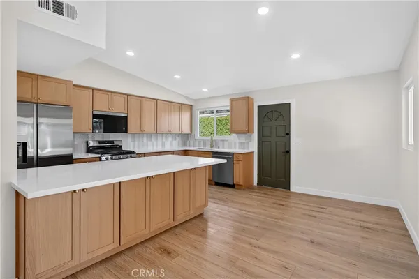 a kitchen with stainless steel appliances granite countertop a stove top oven a sink dishwasher and a refrigerator with wooden floor