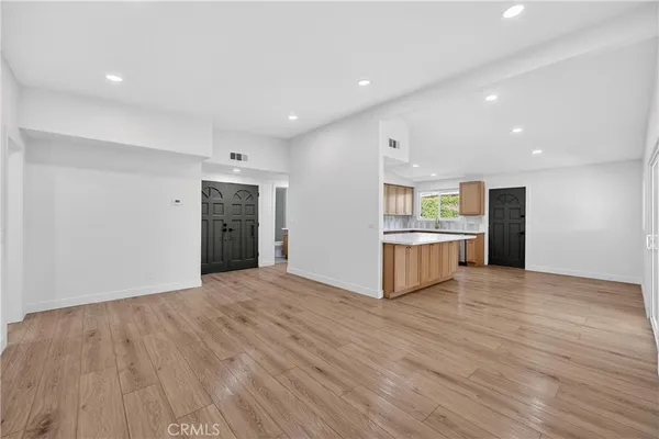 a view of an empty room with wooden floor and a kitchen