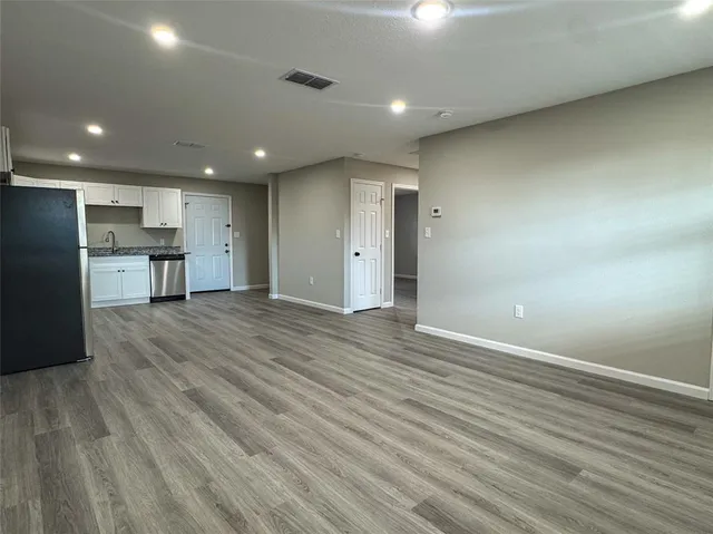 an empty room with wooden floor and a kitchen