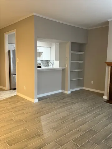 a view of empty room with wooden floor and kitchen