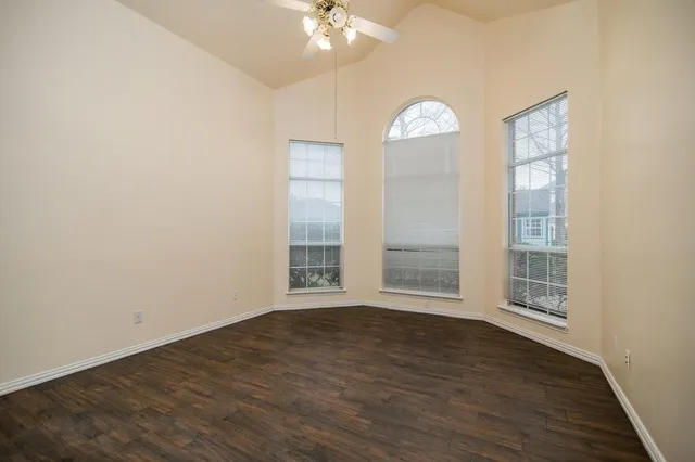 an empty room with wooden floor fan and windows