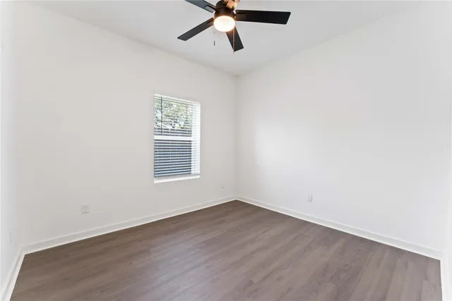 an empty room with wooden floor ceiling fan and window