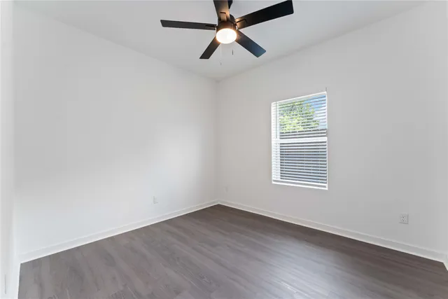 an empty room with wooden floor ceiling fan and windows