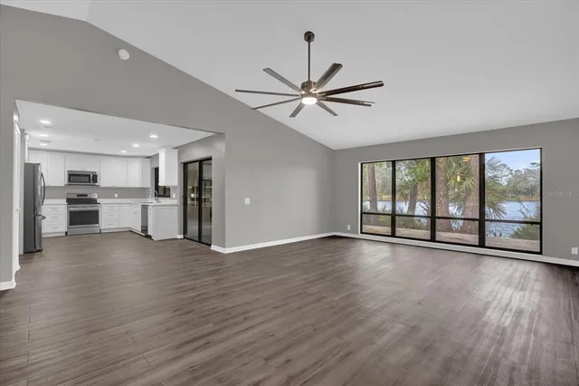 a view of an empty room with wooden floor and a kitchen
