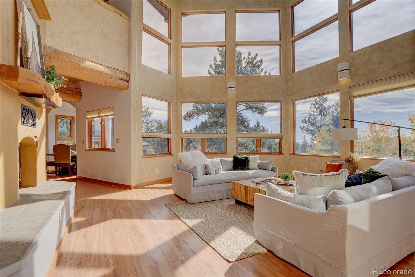 12227 Calfee Gulch Road Conifer, CO 80433 - Photo 9 of 43 a living room with furniture large windows a rug and a chandelier