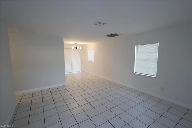 a view of an empty room with window and chandelier fan