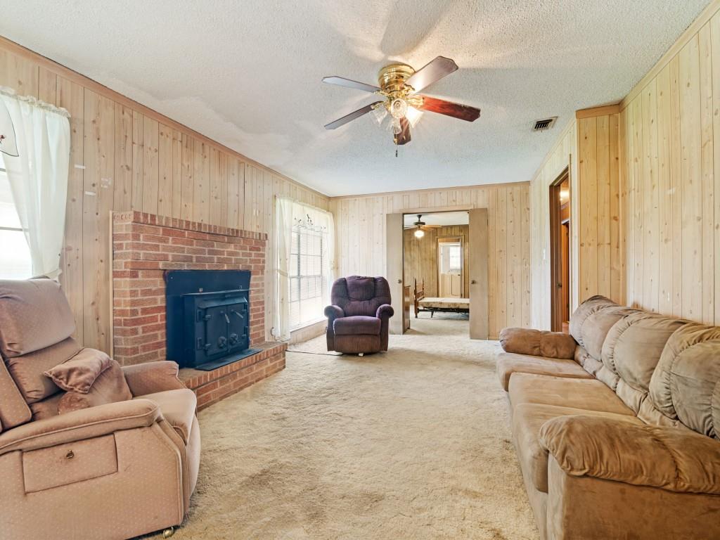 1081 Wright Street Terrell, TX 75160 - Photo 7 of 29 Living area featuring a brick fireplace with a wood-burning insert, wood-paneled walls, carpet flooring, and a ceiling fan