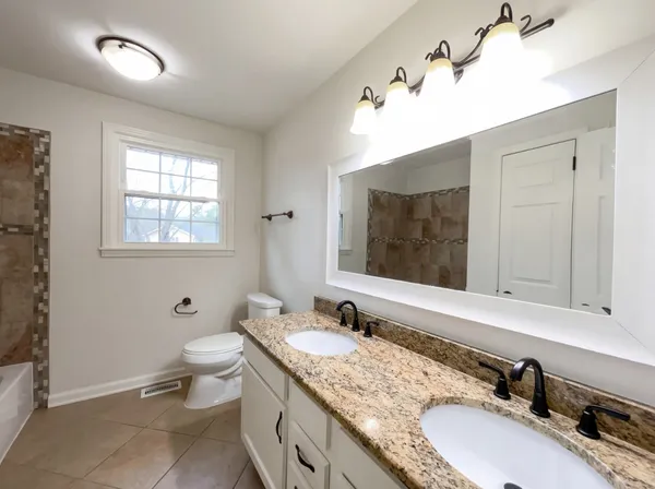 a bathroom with a granite countertop double vanity sink mirror and toilet