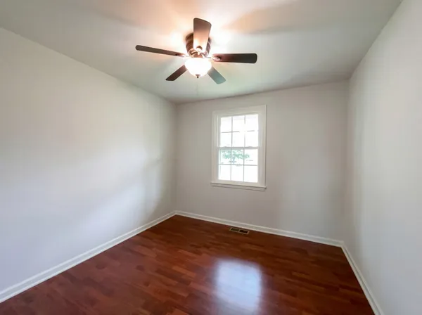 an empty room with wooden floor fan and windows
