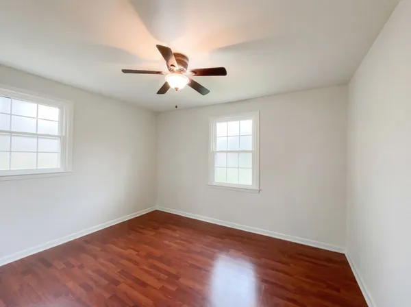 an empty room with wooden floor fan and windows