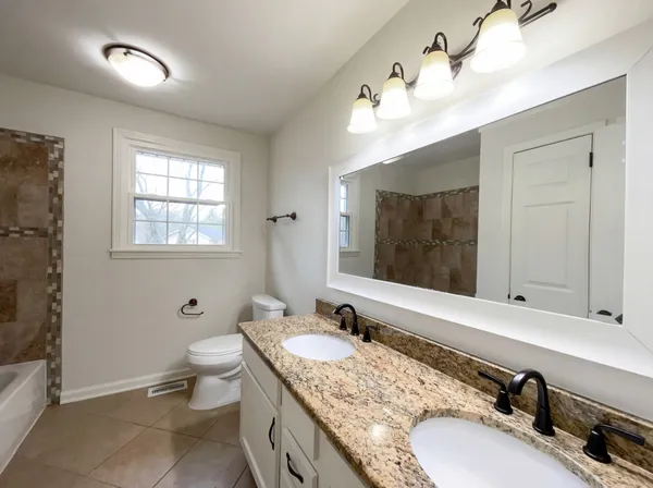 a bathroom with a granite countertop double vanity sink a mirror and a toilet