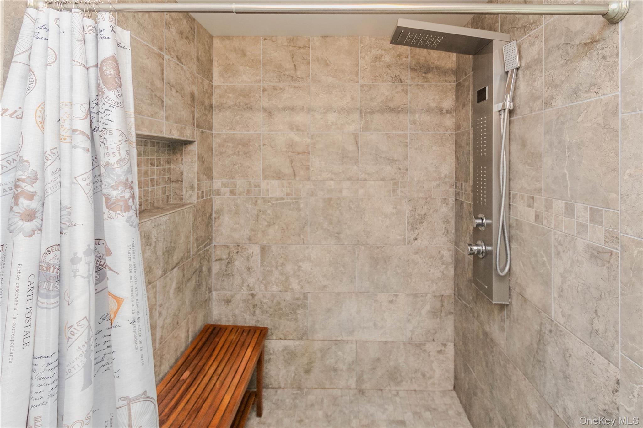 15 Van Dewark Road Middletown, NY 10941 - Photo 18 of 41 Shower stall featuring large format tile walls, a built-in niche with mosaic tile accents, a multi-function shower panel with an overhead rain shower and handheld sprayer, and a slatted wood bench