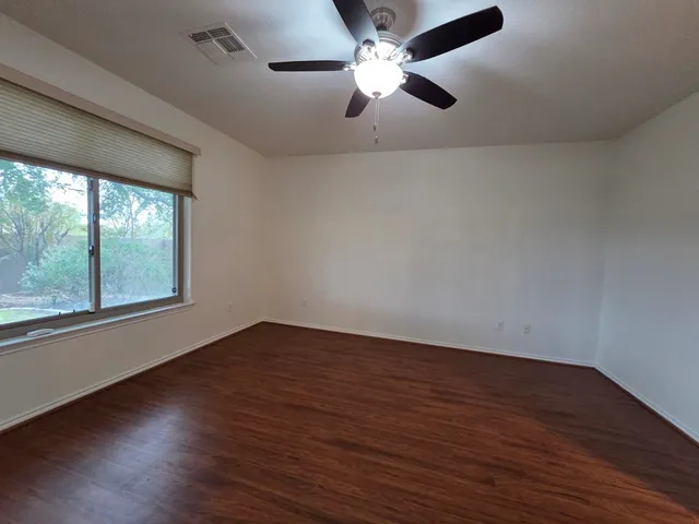 an empty room with wooden floor fan and windows