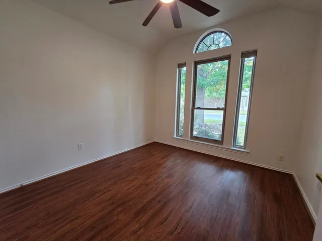 an empty room with wooden floor chandelier and windows
