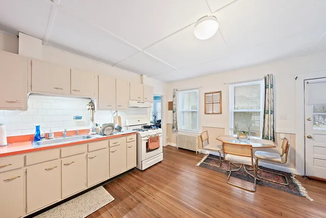 a kitchen with a sink dishwasher a dining table chairs refrigerator and cabinets with wooden floor