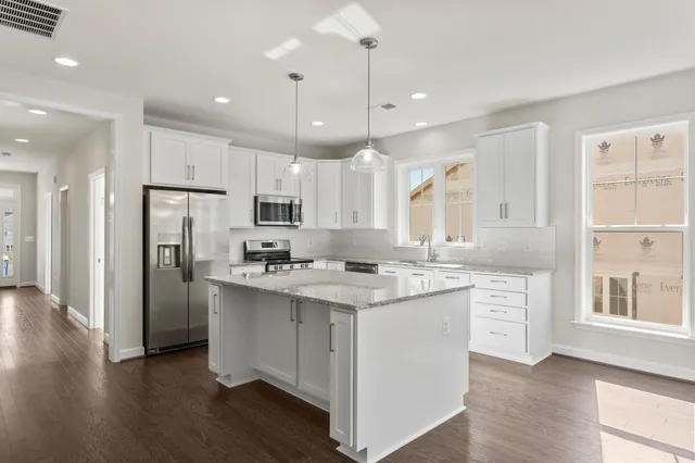 a kitchen with stainless steel appliances granite countertop a refrigerator a sink dishwasher a oven and a dining table with wooden floor