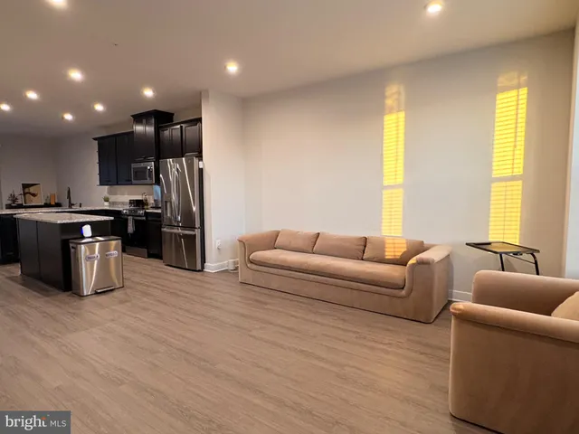 a living room with stainless steel appliances kitchen island granite countertop a couch and a refrigerator