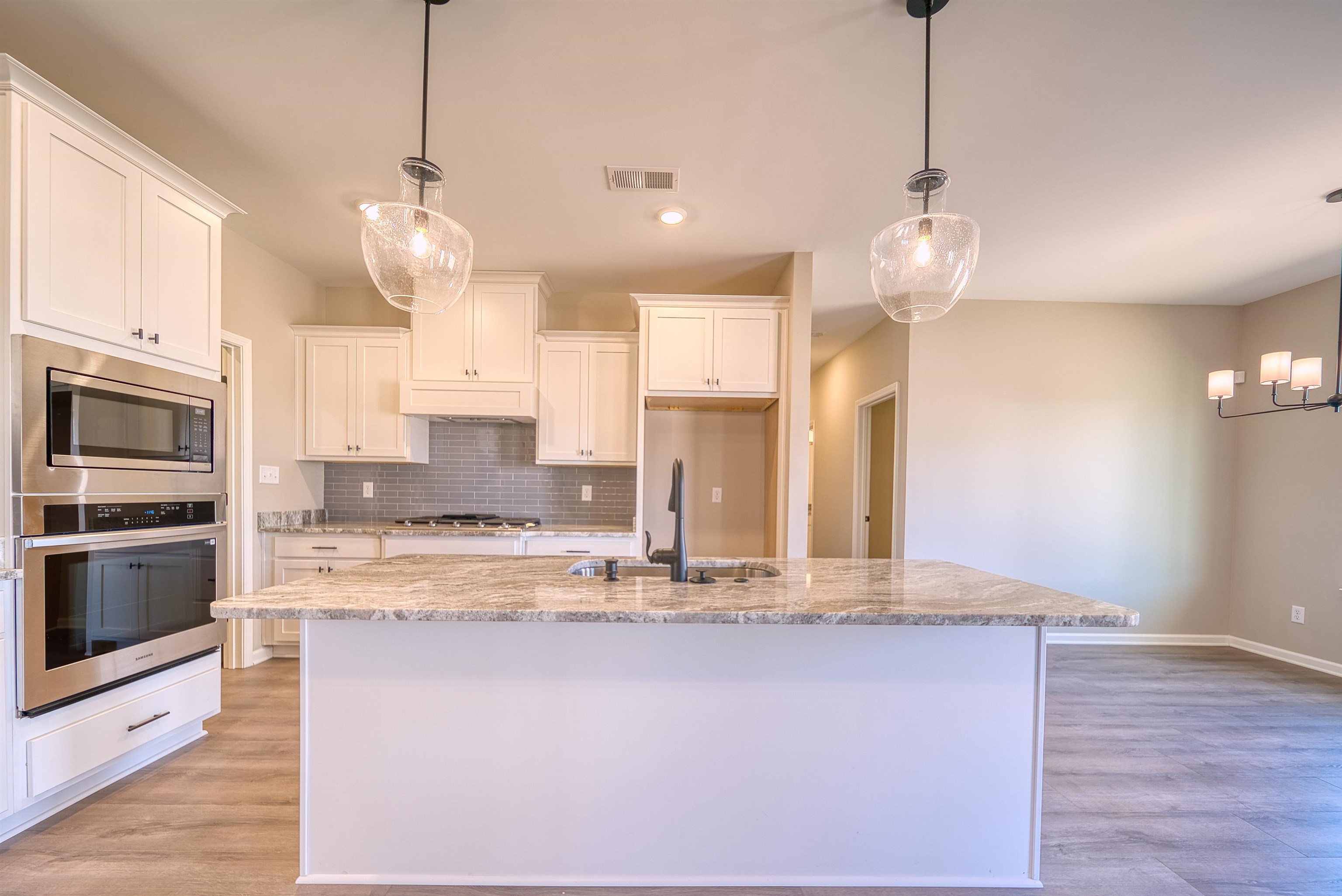 19 Columbia Way Atoka, TN 38004 - Photo 9 of 40 Kitchen featuring hanging light fixtures, stainless steel appliances, light stone countertops, white cabinetry, and light wood-style flooring