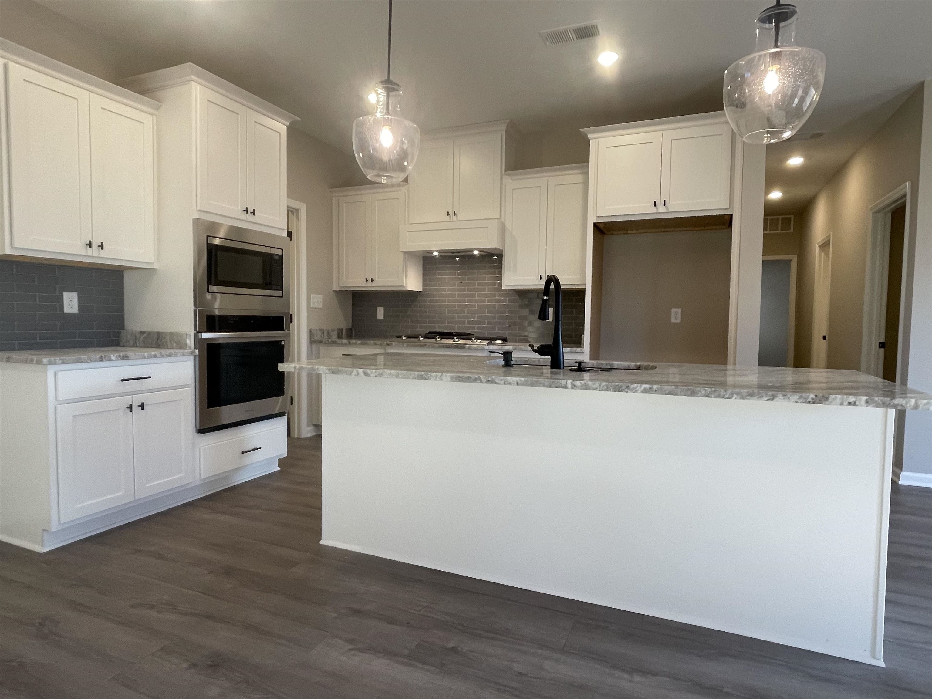 19 Columbia Way Atoka, TN 38004 - Photo 9 of 28 Kitchen with light stone counters, white cabinetry, stainless steel appliances, hanging light fixtures, and a center island with sink