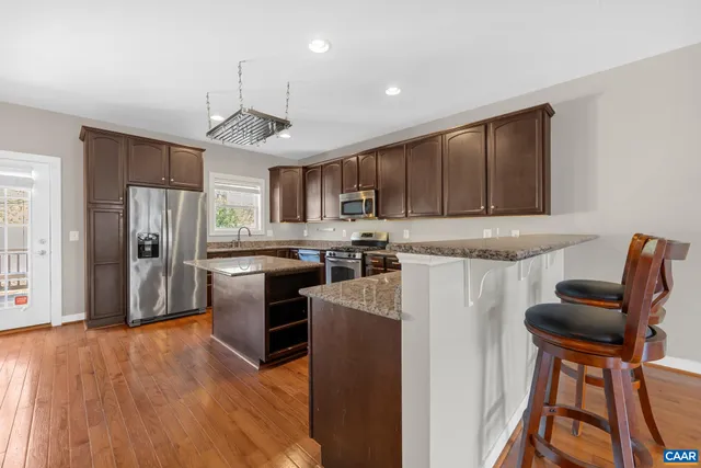 a kitchen with stainless steel appliances granite countertop a refrigerator a stove top oven a sink dishwasher and white cabinets with wooden floor