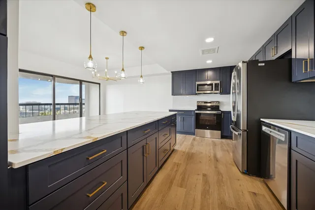 a large kitchen with stainless steel appliances kitchen island granite countertop a large kitchen island a stove a refrigerator a sink and dishwasher with wooden floor