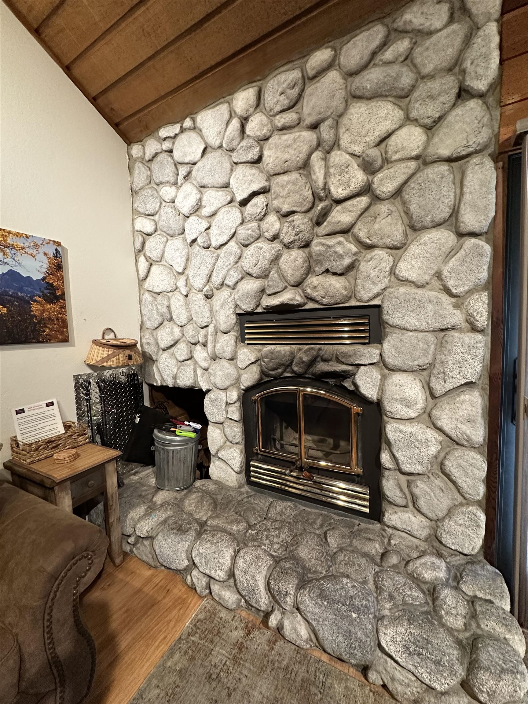 315 Fascination, Unit 315 Mammoth Lakes, CA 93546 - Photo 37 of 44 Stone fireplace with a black framed inset firebox, stone hearth, wood-finish flooring, and a natural wood plank ceiling