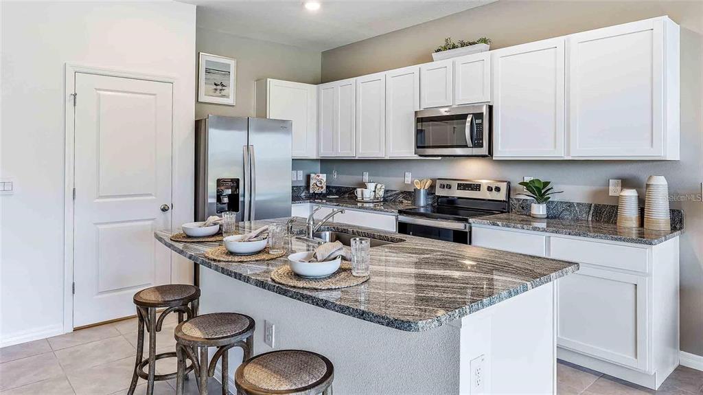32395 Turtle Grace Loop Wesley Chapel, FL 33545 - Photo 31 of 39 a kitchen with a sink a stove and chairs with kitchen island