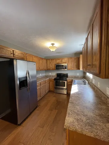 a kitchen with stainless steel appliances granite countertop a refrigerator a stove and a sink with wooden floor