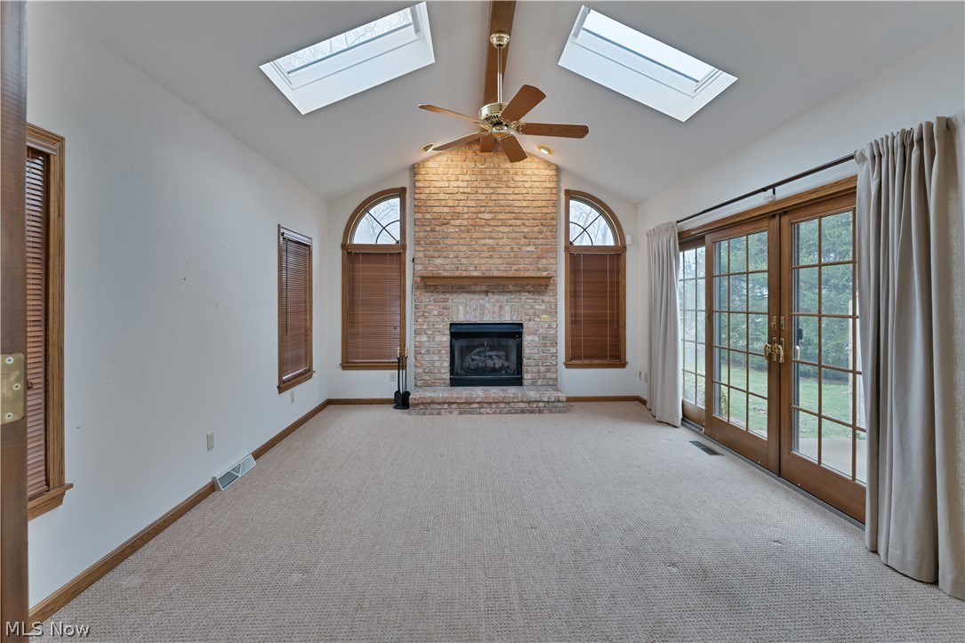 6599 Struthers Road Youngstown, OH 44514 - Photo 15 of 29 Unfurnished living room featuring carpet, french doors, a skylight, a fireplace, and a ceiling fan