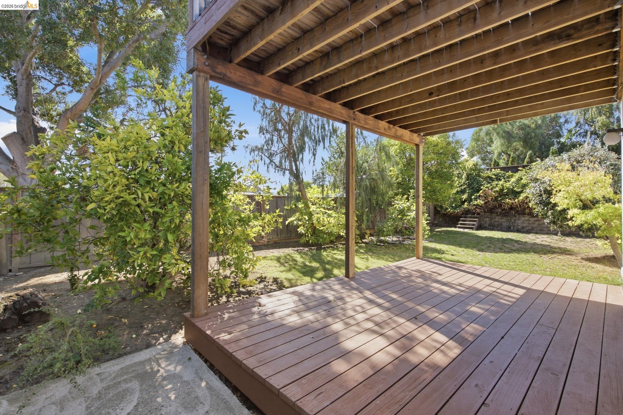 4522 Santa Rita Road El Sobrante, CA 94803 - Photo 45 of 58 Covered wooden deck with exposed beam ceiling, overlooking a grassy yard with mature trees and a sloped, planted area