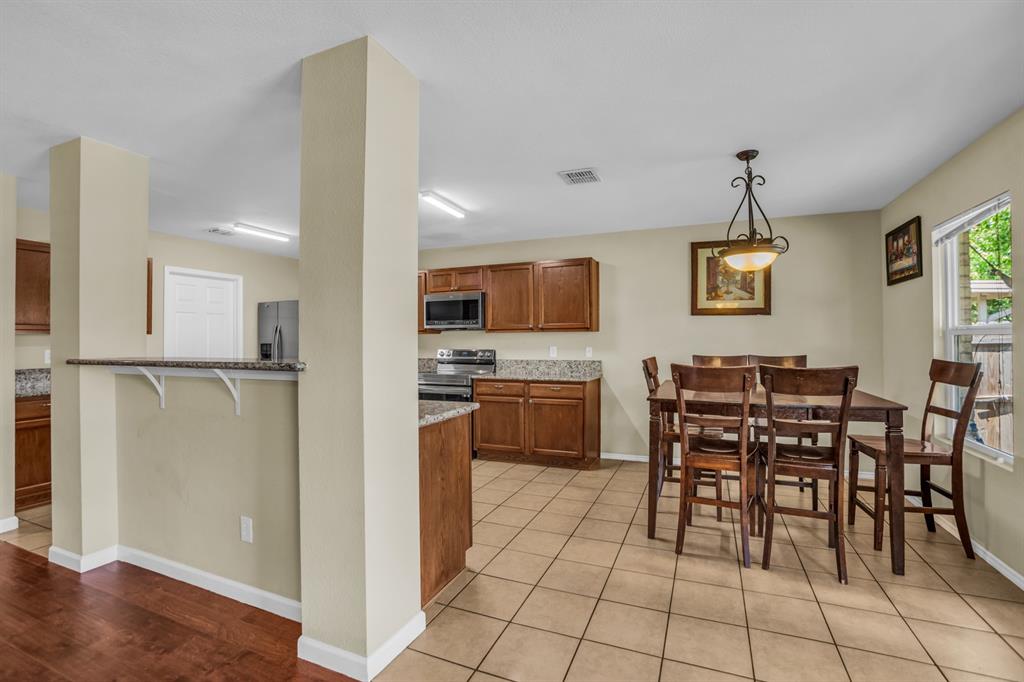 5718 Green Ivy Road Denton, TX 76210 - Photo 9 of 37 Kitchen and dining area featuring warm wood cabinetry, neutral countertops, stainless steel appliances, and a tiled floor