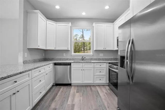 a kitchen with granite countertop a stove a sink and white cabinets with wooden floor next to windows