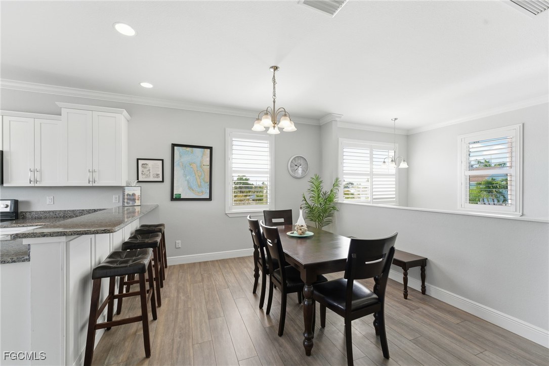 12304 Boat Shell Drive Matlacha Isles, FL 33991 - Photo 32 of 49 a dining room with wooden floor a chandelier a wooden table and chairs