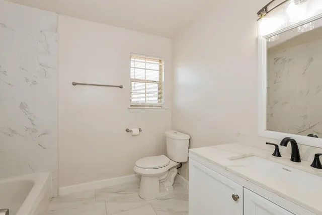 a bathroom with a granite countertop toilet a sink a mirror and a window