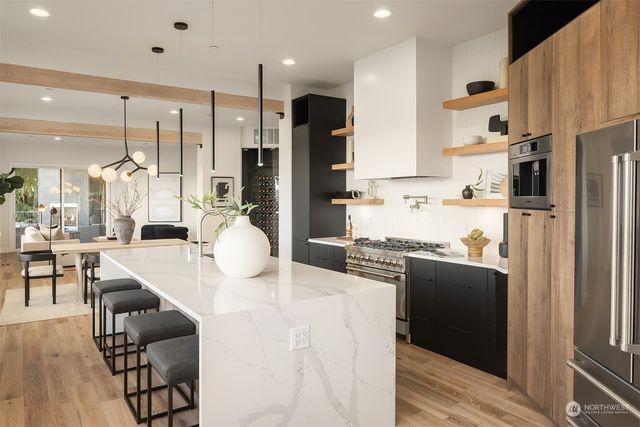 a kitchen with stainless steel appliances kitchen island granite countertop a refrigerator a stove a sink a dining table and chairs with wooden floor