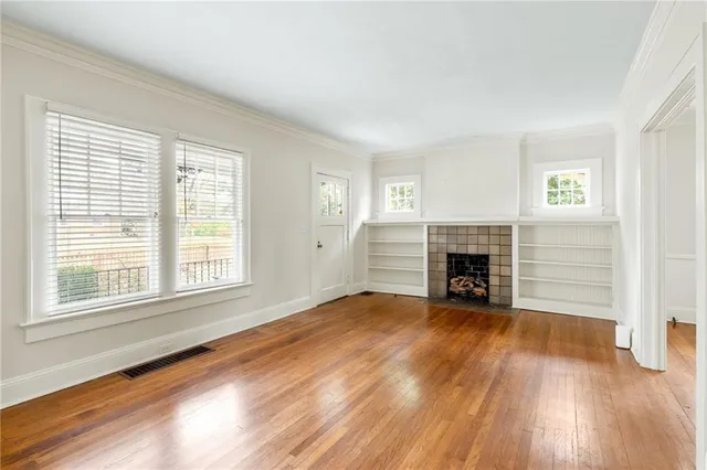 an empty room with wooden floor fireplace and windows