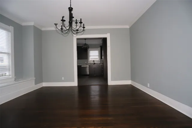 an empty room with wooden floor chandelier and windows