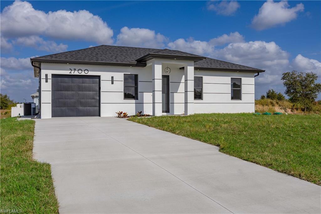 View of front facade with a front yard, a garage, driveway, stucco siding, and roof with shingles