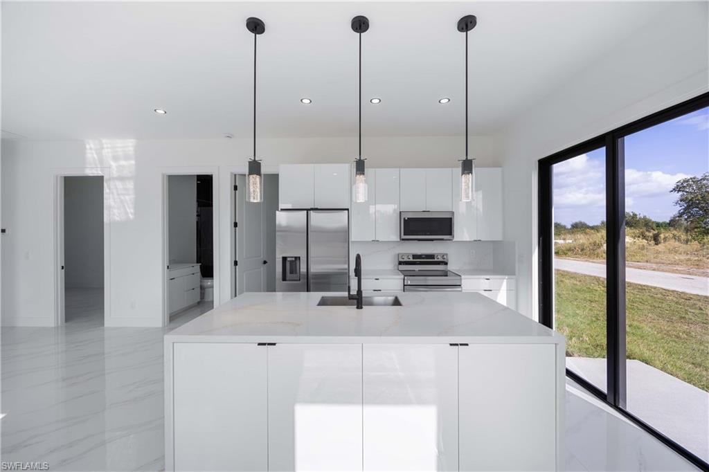 2700 49th Street Southwest Lehigh Acres, FL 33976 - Photo 11 of 24 Kitchen with appliances with stainless steel finishes, light stone counters, pendant lighting, an island with sink, and white cabinets