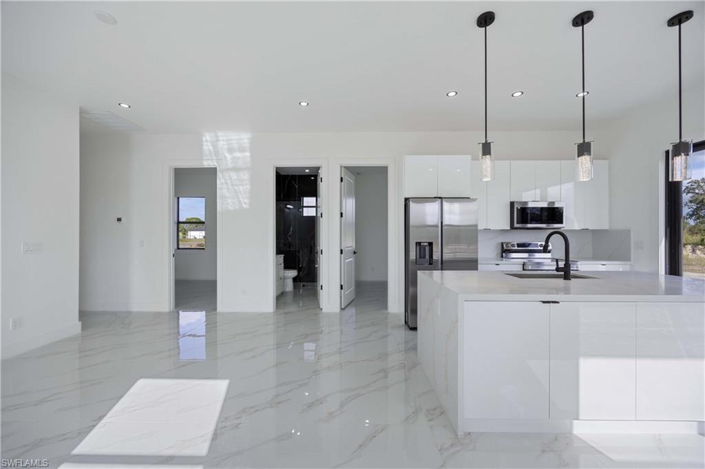 2700 49th Street Southwest Lehigh Acres, FL 33976 - Photo 14 of 24 Kitchen featuring white cabinets, modern cabinets, stainless steel appliances, decorative light fixtures, and light stone counters