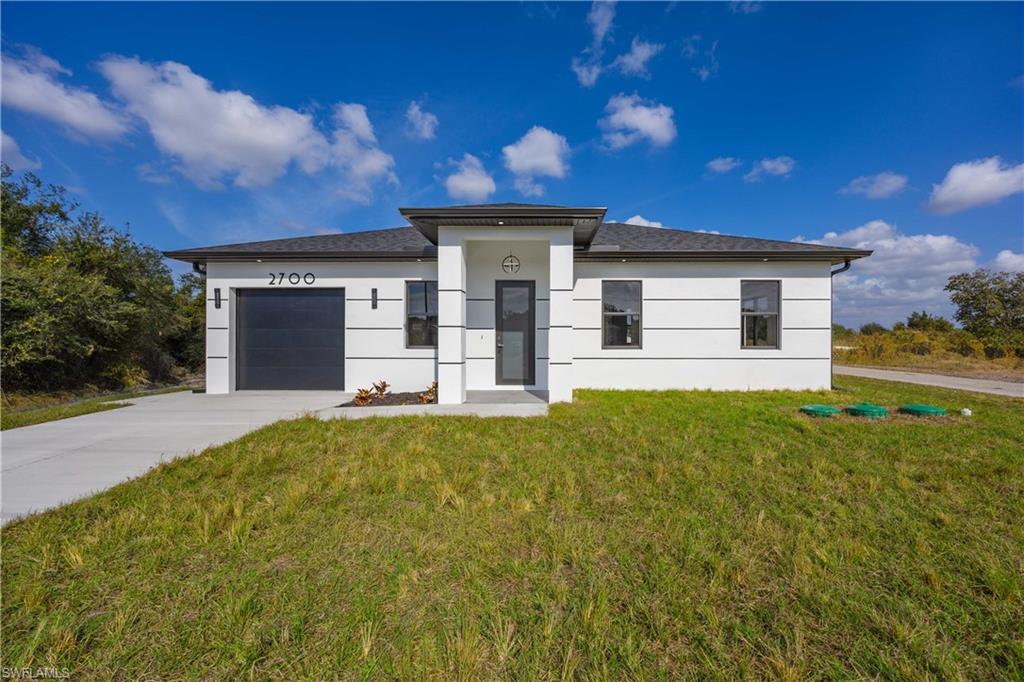 2700 49th Street Southwest Lehigh Acres, FL 33976 - Photo 2 of 24 Prairie-style house featuring an attached garage, driveway, a front yard, and stucco siding