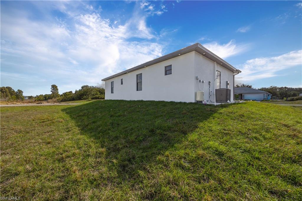 2700 49th Street Southwest Lehigh Acres, FL 33976 - Photo 24 of 24 View of side of home featuring stucco siding and a lawn