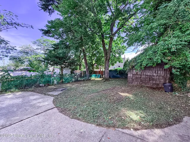 a view of a backyard with large trees and a small barn