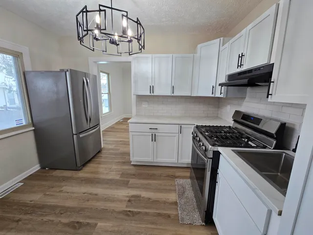 a kitchen with stainless steel appliances granite countertop a refrigerator a stove a sink dishwasher and white cabinets with wooden floor