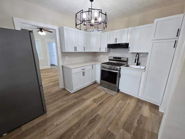 a kitchen with granite countertop a refrigerator stove and white cabinets