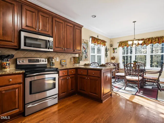 a kitchen with stainless steel appliances granite countertop a stove top oven a sink dishwasher a dining table and chairs with wooden floor