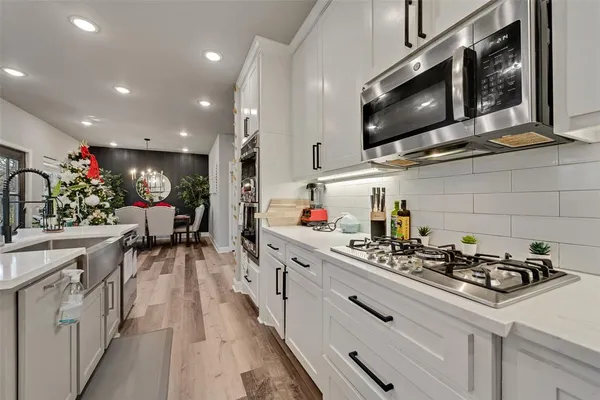 a kitchen with stainless steel appliances kitchen island granite countertop a sink dishwasher a microwave oven a stove and white cabinets with wooden floor